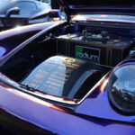 A purple sports car with its hood open, displaying a detailed engine compartment with various labels and a radium air filter, ready for a cars+coffee event.