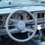 Vintage car dashboard featuring a blue steering wheel, speedometer, tachometer, and a central console with air vents at a cars+coffee event.