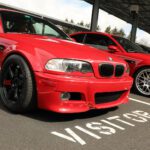 Red bmw m3 parked in a visitor area at a cars+coffee event with another bmw in the background.