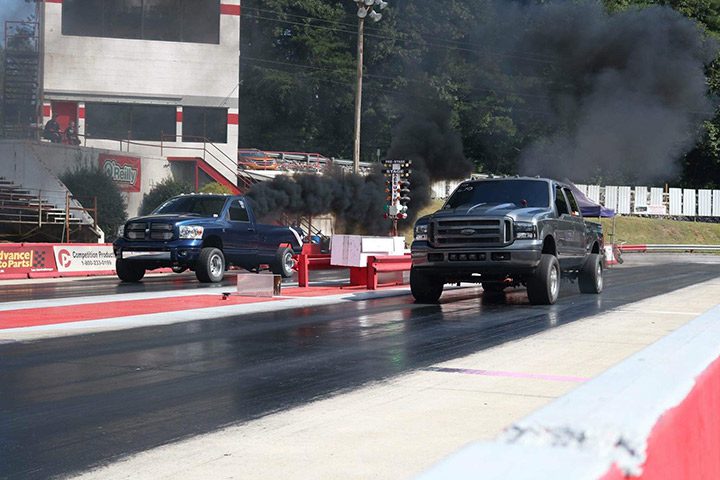 Two trucks on a track with smoke coming out of them.