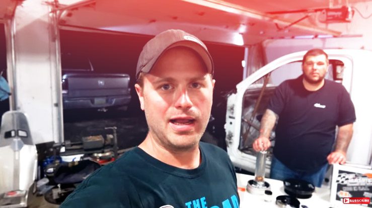 Two men standing in front of a truck in a garage.